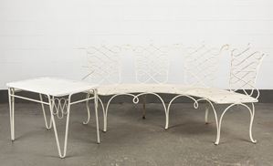 A semi-circular white wrought iron garden sofa and coffee table
