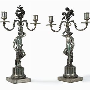 Pair of silver candlesticks representing male and female figures on half-column bases supporting vases of flowers, early 20th century