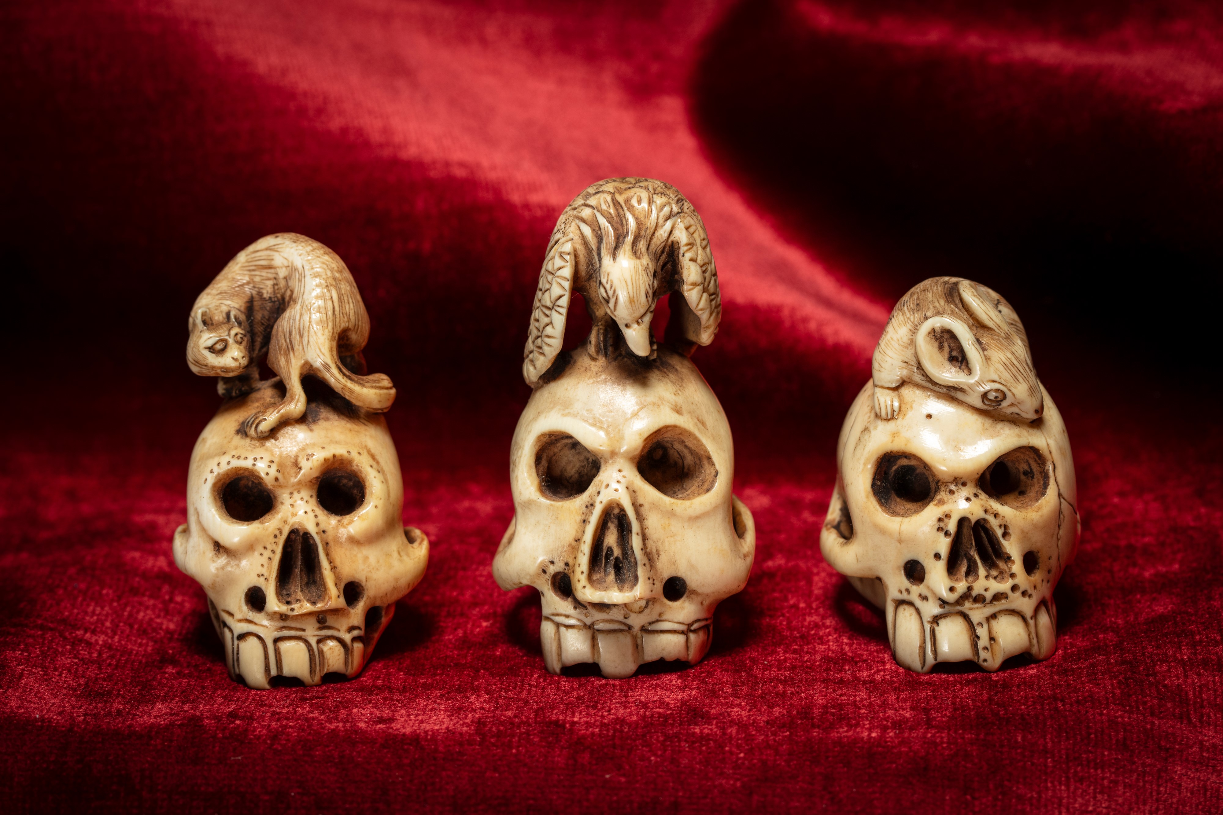 Three carved and pierced ivory skull-shaped netsuke, surmounted by