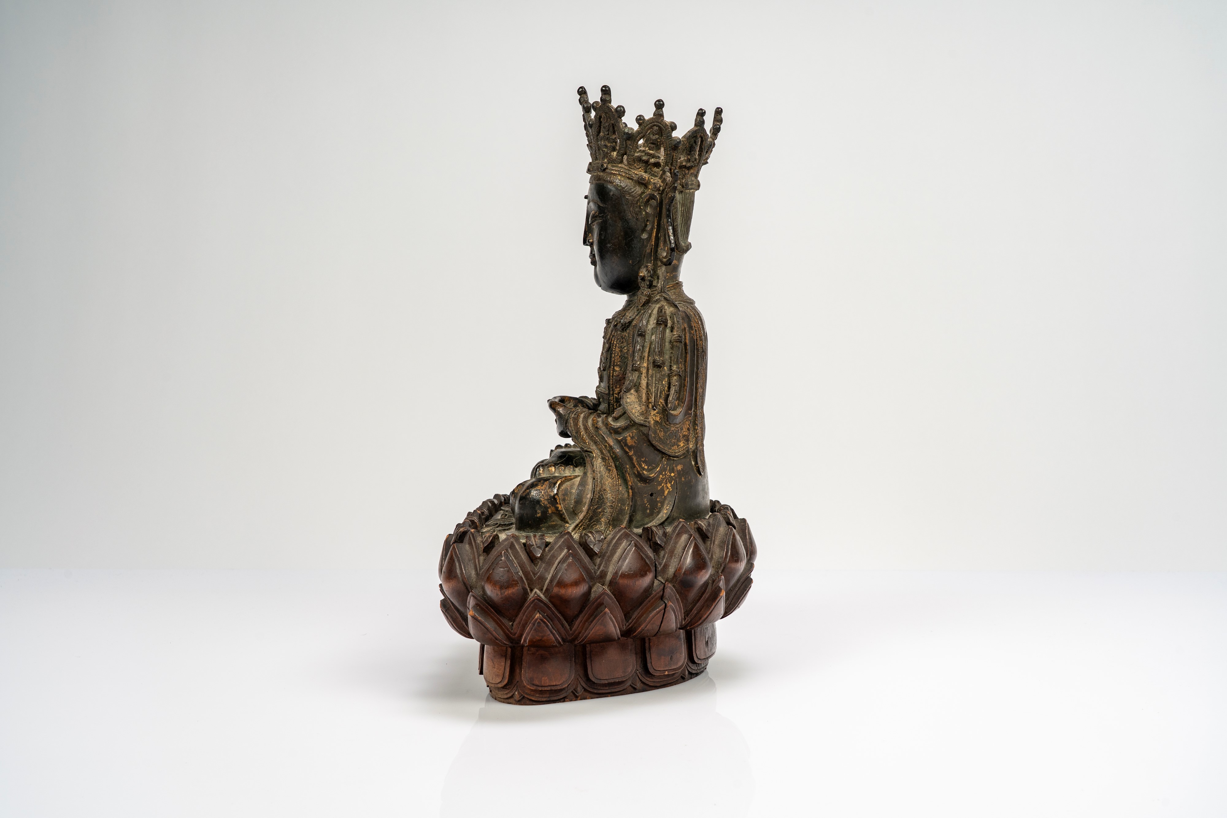 Guanyin in bronzo cesellato, con tracce di doratura, su base lignea a fiori di loto di epoca succ...
