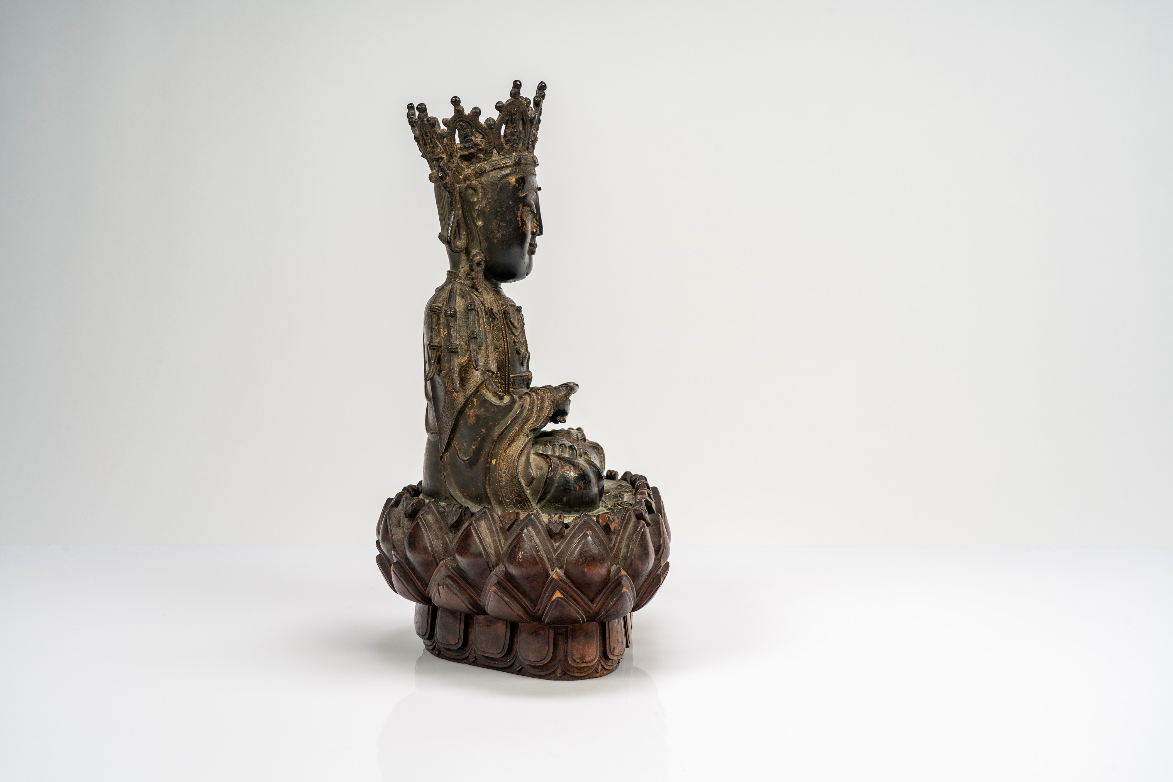 Guanyin in bronzo cesellato, con tracce di doratura, su base lignea a fiori di loto di epoca succ...