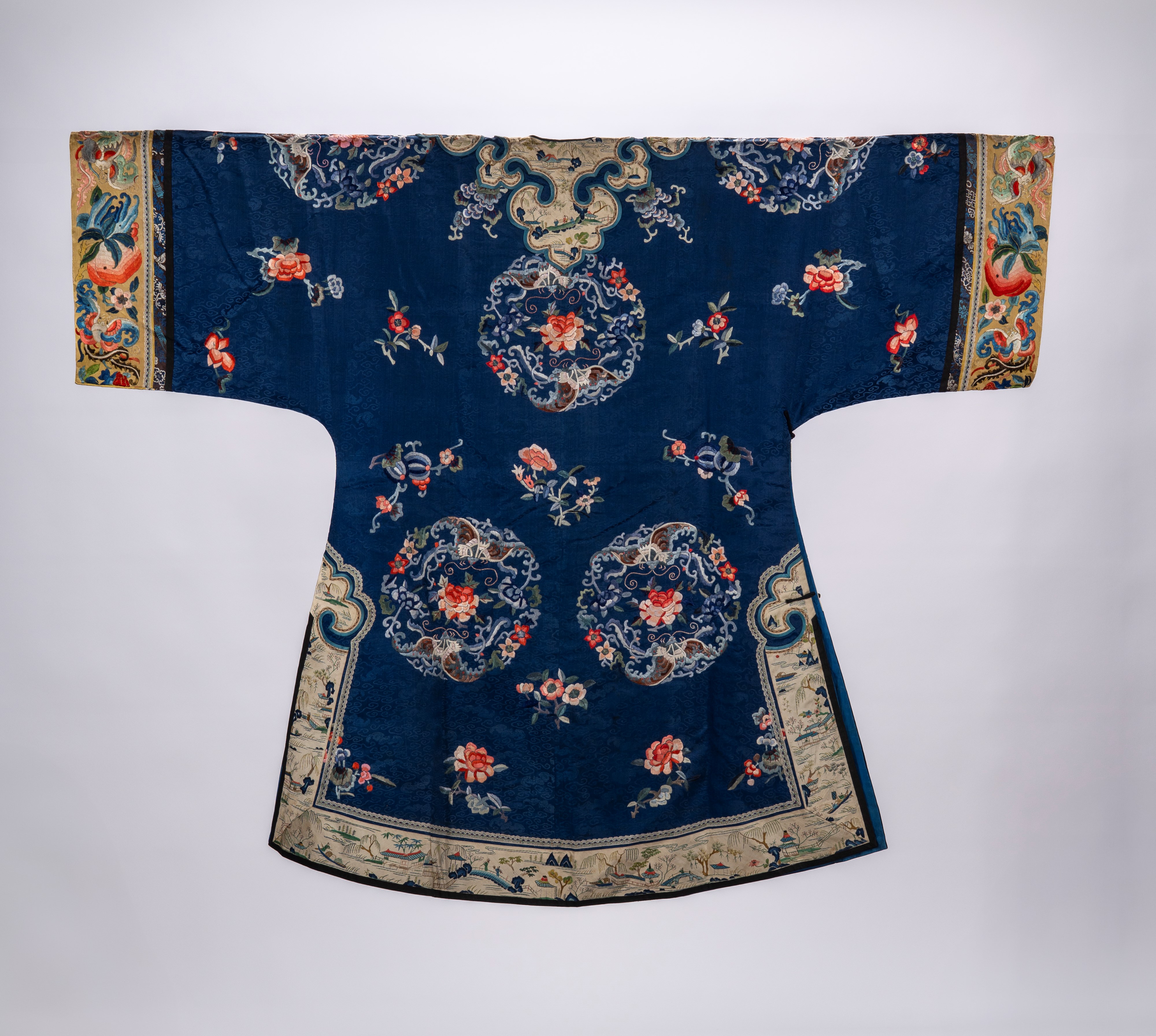 Lotto di due vesti in seta a fondo blu, una decorata con motivi floreali, ruyi e figure, l’altra ...