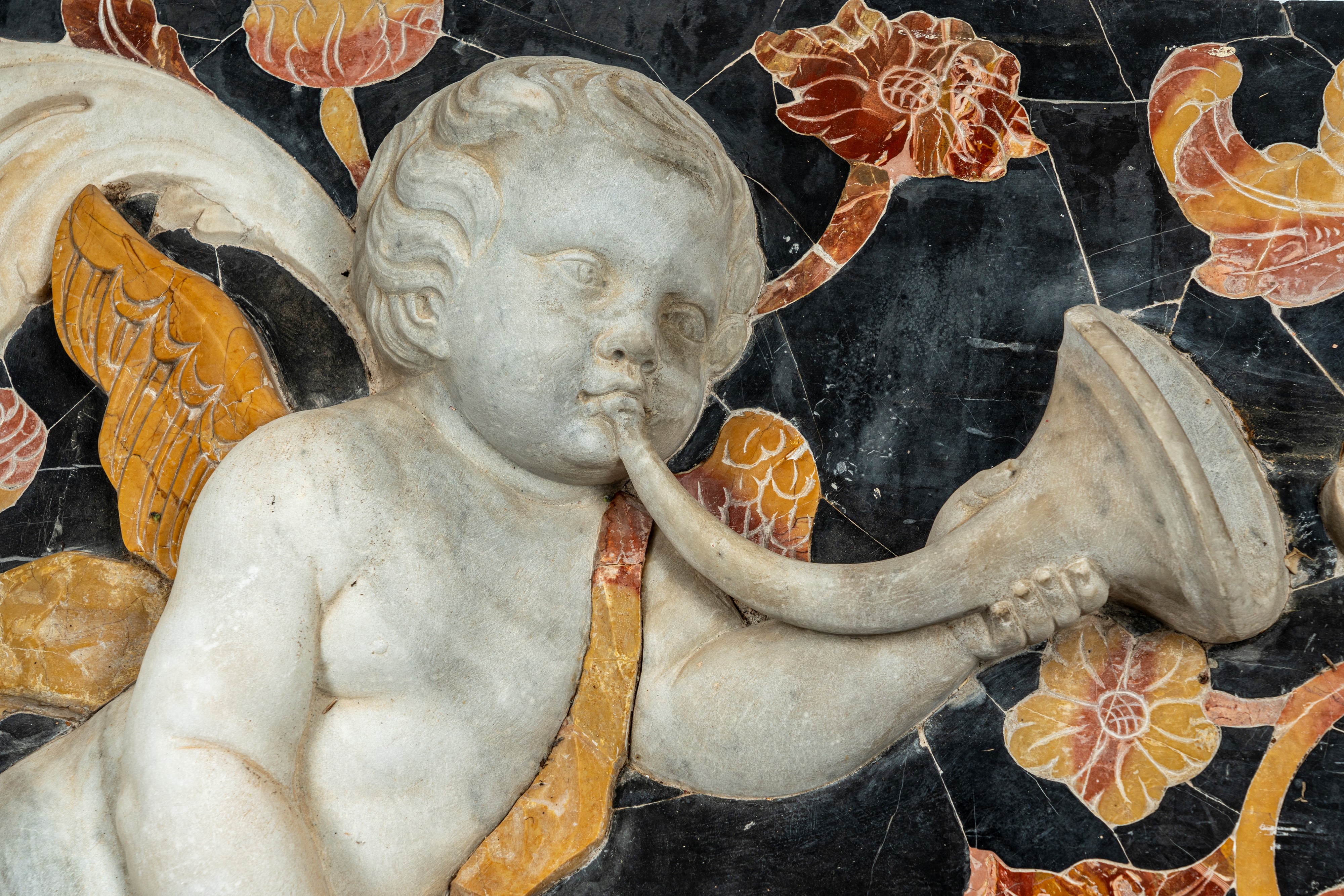 Importante pannello a tecnica mista in marmo scolpito e intarsiato raffigurante putto tra girali ...