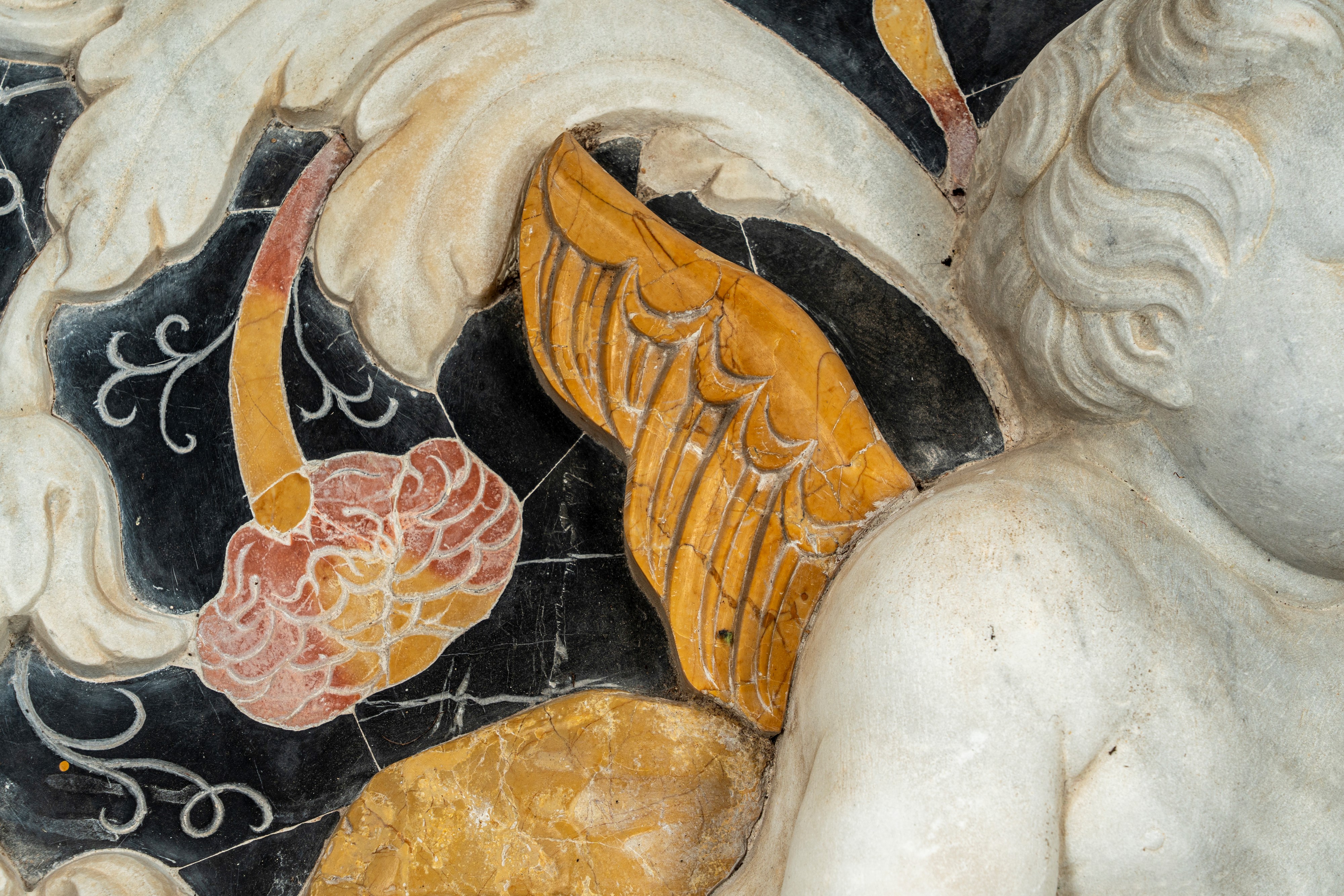 Importante pannello a tecnica mista in marmo scolpito e intarsiato raffigurante putto tra girali ...