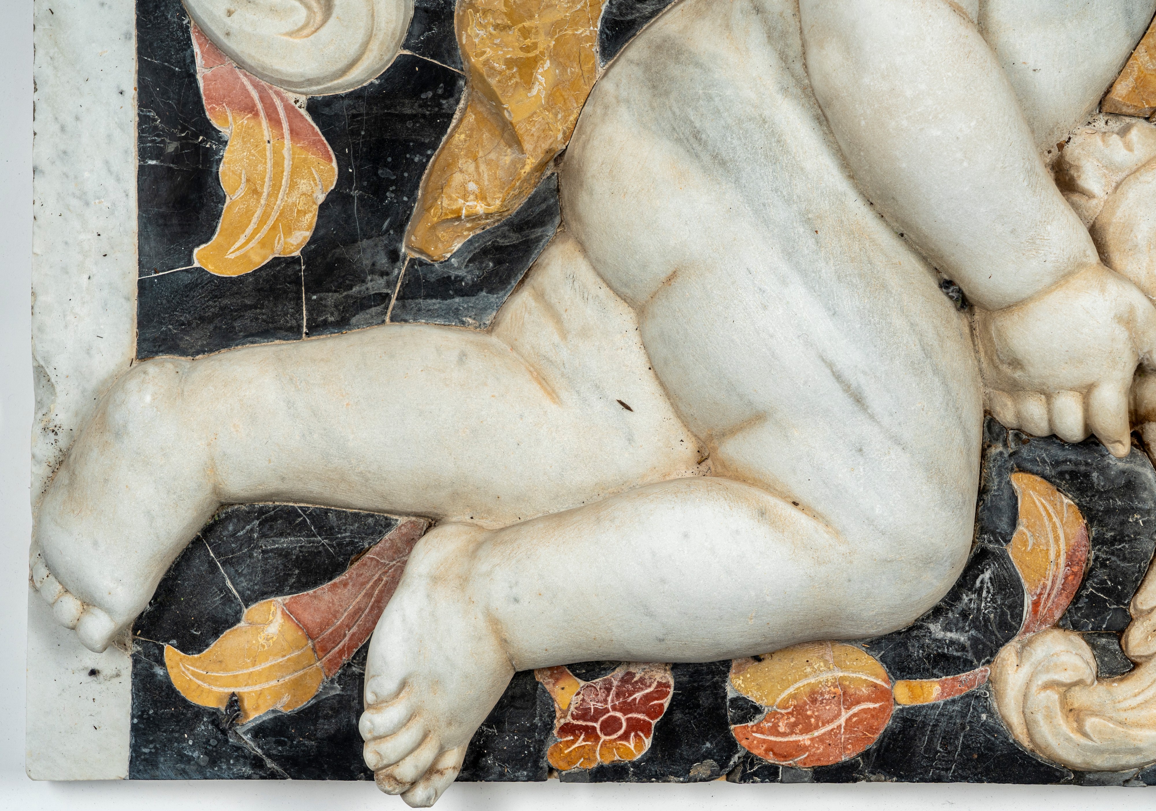 Importante pannello a tecnica mista in marmo scolpito e intarsiato raffigurante putto tra girali ...