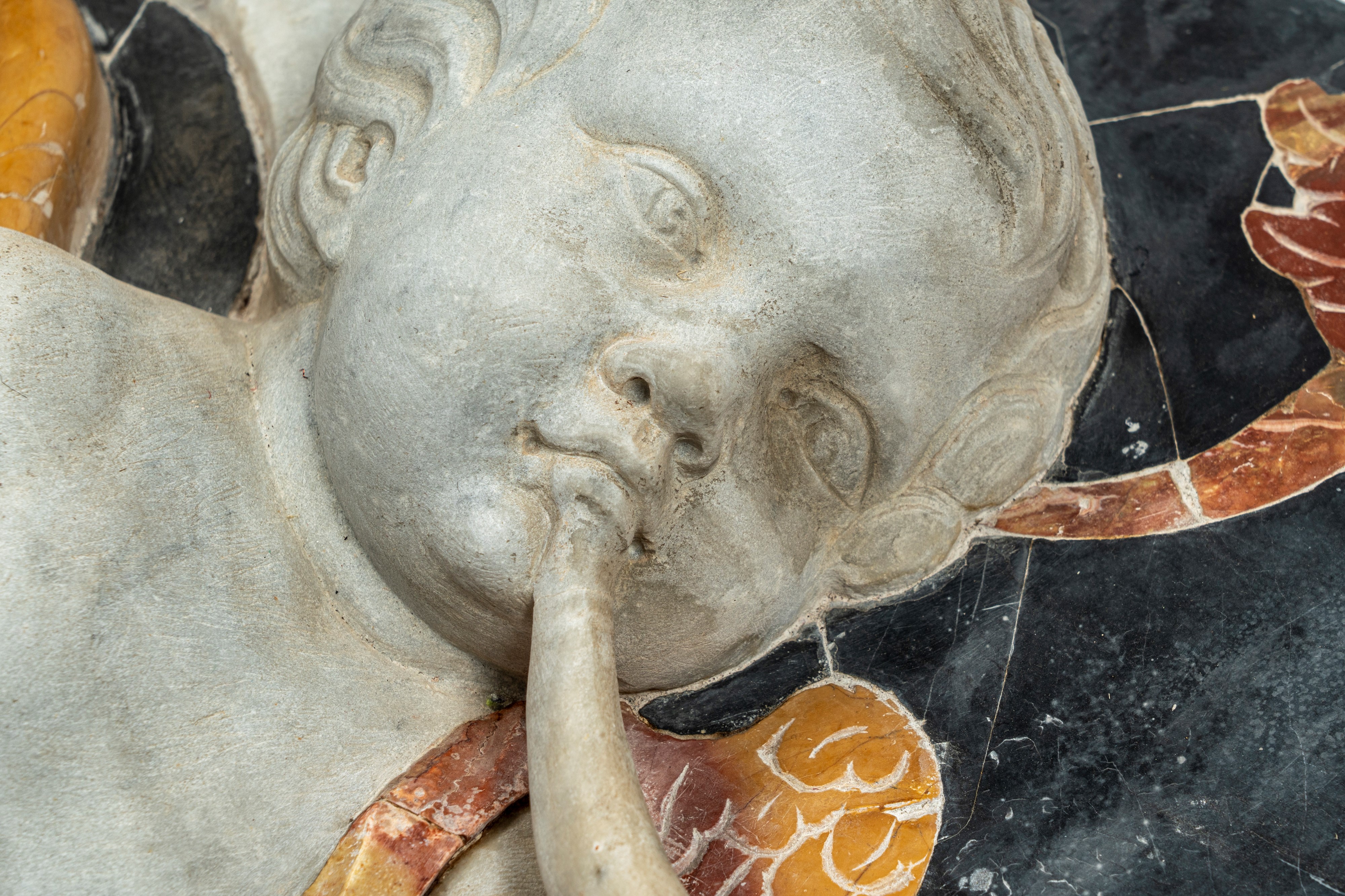 Importante pannello a tecnica mista in marmo scolpito e intarsiato raffigurante putto tra girali ...