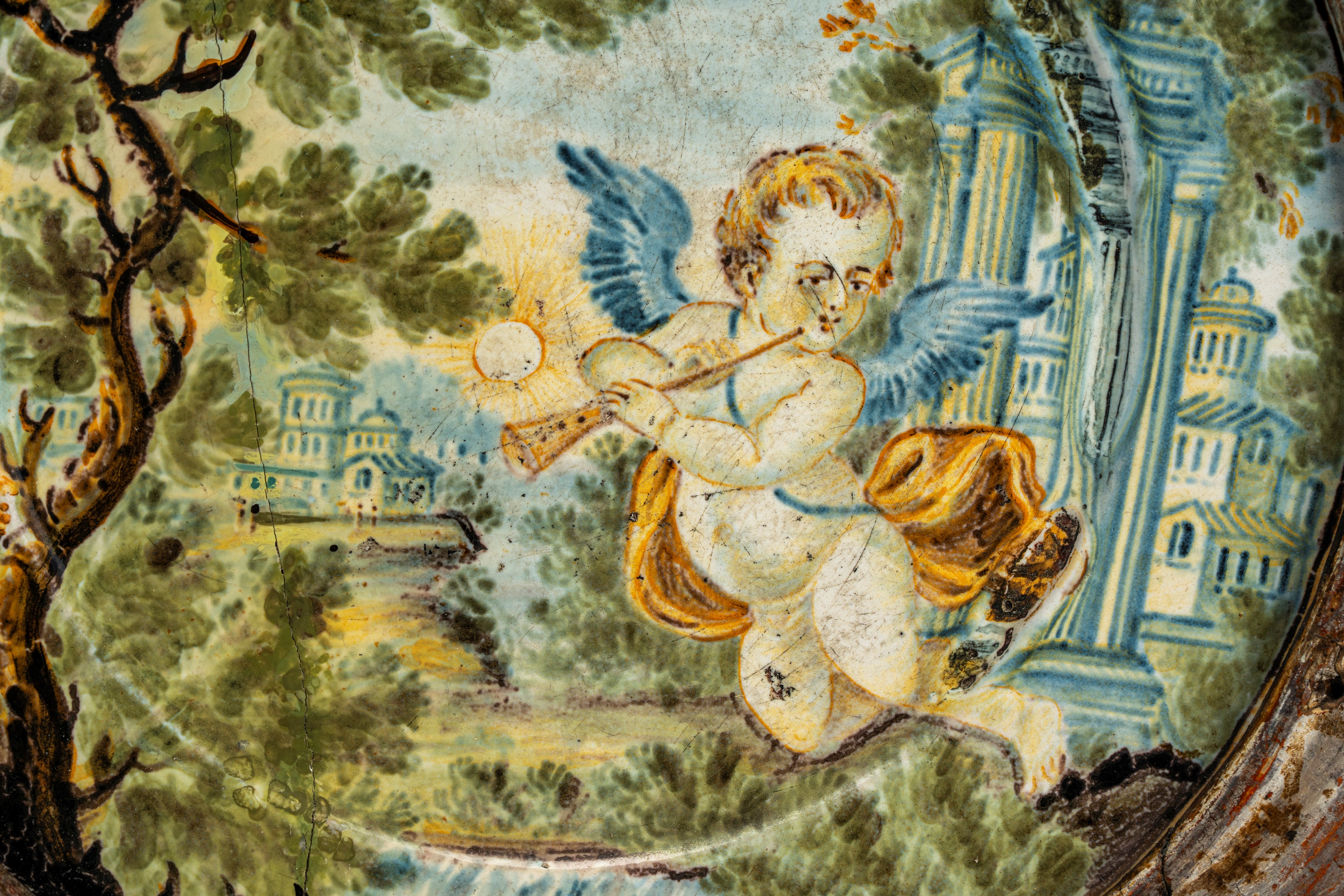 Piattello in maiolica policroma istoriata con putto alato musicante in un paesaggio agreste con s...