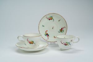 Pair of porcelain cups with saucers, gilt-edged and painted in polychrome with bouquets and scattered flowers. Probably French manufactory, late 18th century