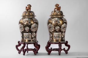 Coppia di potiche in porcellana decorate con scene di vita quotidiana entro pannelli su fondo nero con oro, coperchio con shishi, Kutani, Giappone. Basi in legno