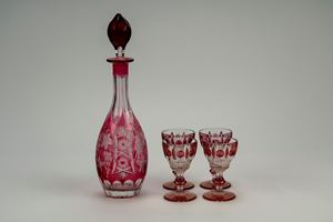 Lotto composto da una brocca in vetro color rubino inciso a tralci d'uva e motivi a stella e quattro piccoli calici in vetro trasparente e color rubino con coppa a motivi geometrici e stelo a balaustro su piede circolare.