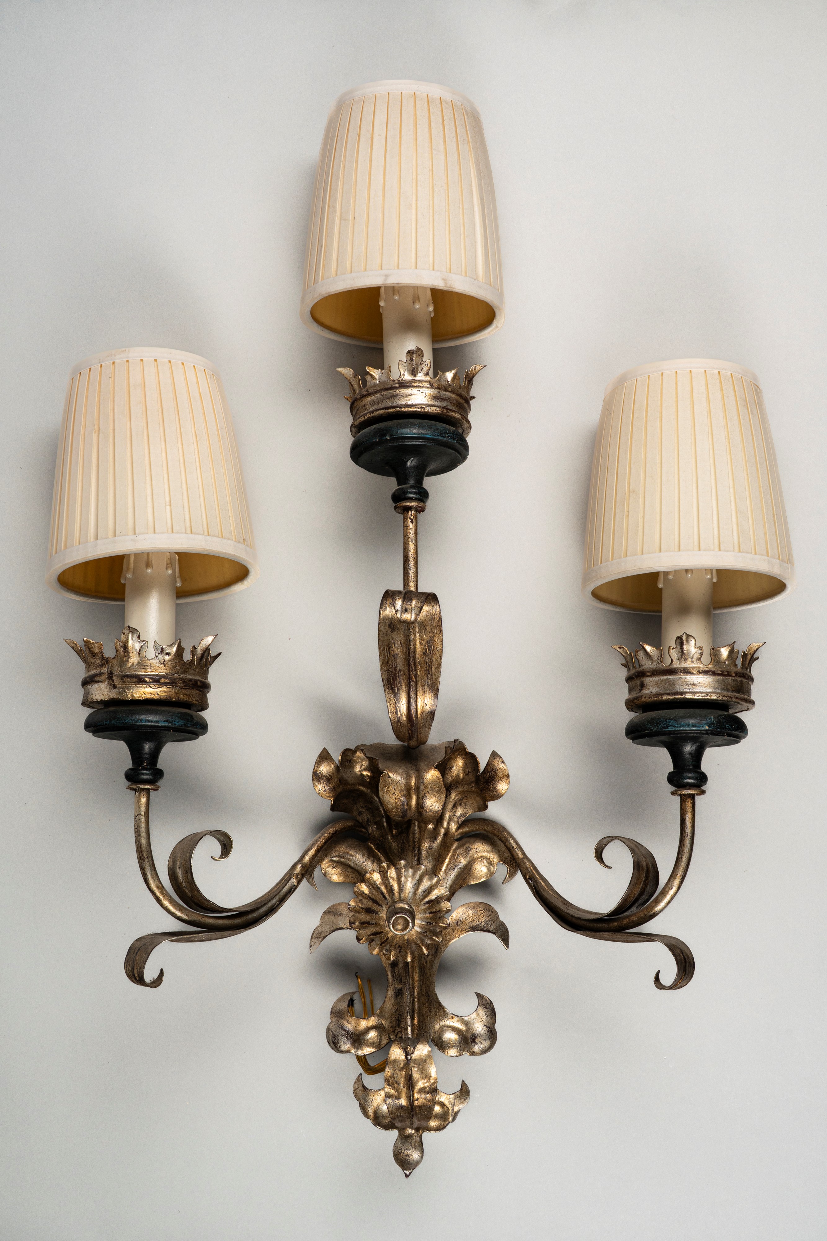 Coppia di appliques, metallo argentato a tre luci con bracci mossi a volute di foglie e fiori