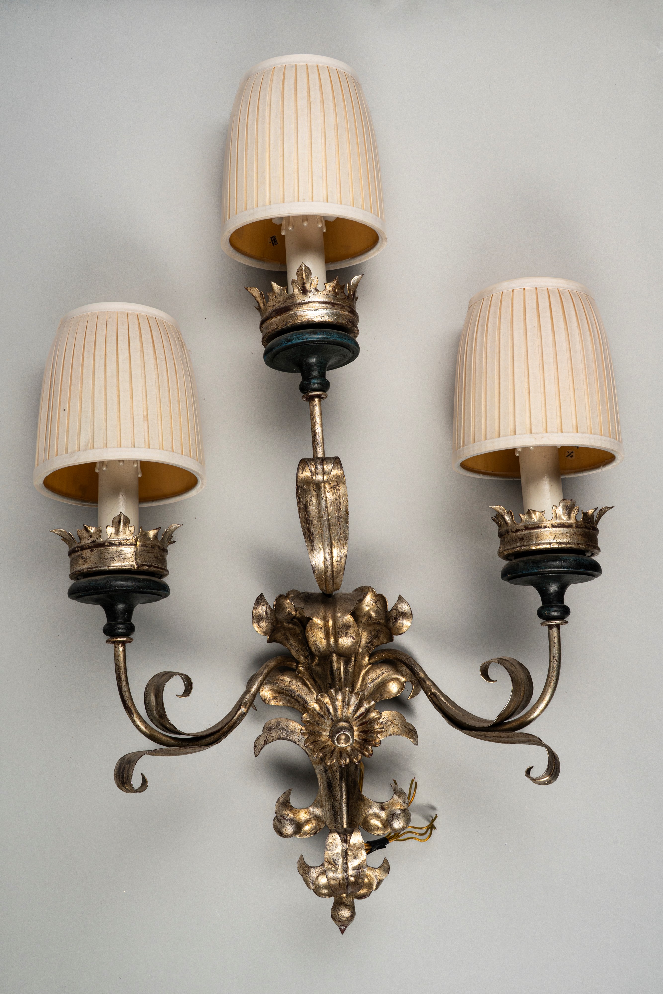 Coppia di appliques, metallo argentato a tre luci con bracci mossi a volute di foglie e fiori