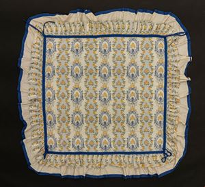 Tovaglia in cotone decorata nei toni del blu dell'azzurro e del giallo a medaglioni e fiori, bordo a balze con nastro azzuro, tessuto G&uuml;ell Lamadrid