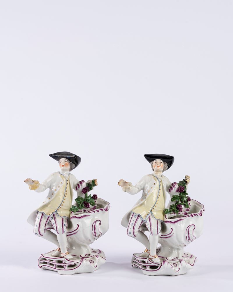 Coppia di saliere in porcellana policroma in forma di gentiluomo, su base a rocaille. Manifattura...