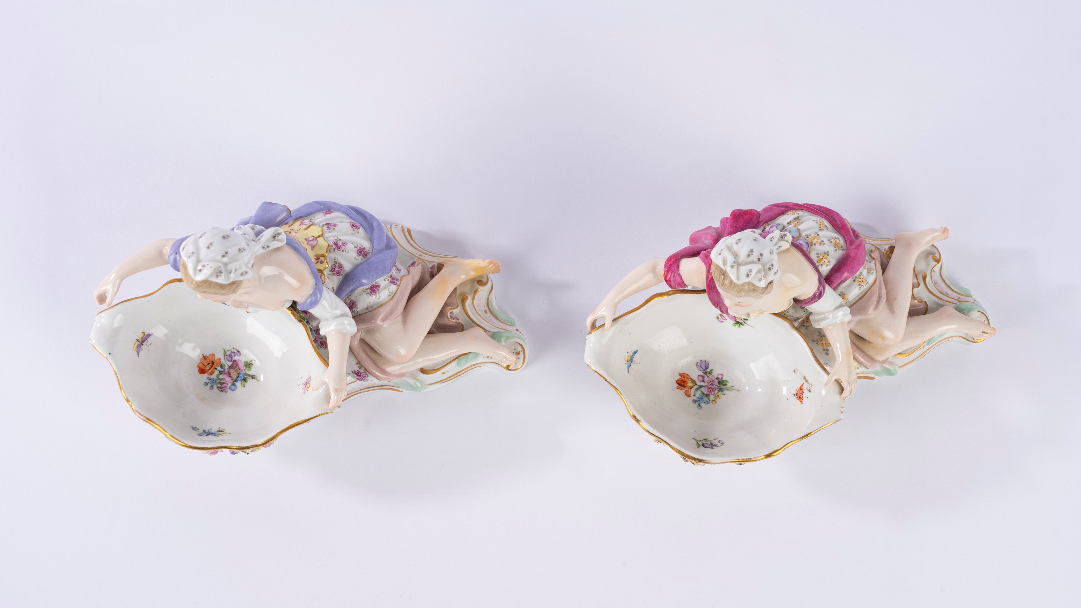 Coppia di saliere o salsiere in porcellana policroma in forma di fanciulla sdraiata che sostiene ...