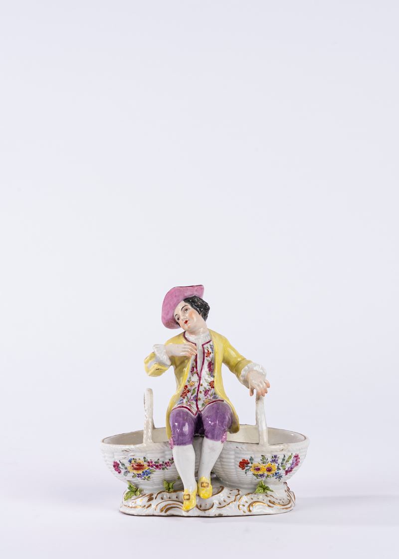 Saliera in porcellana policroma in forma di giovane gentiluomo seduto tra due cestini in finto vi...