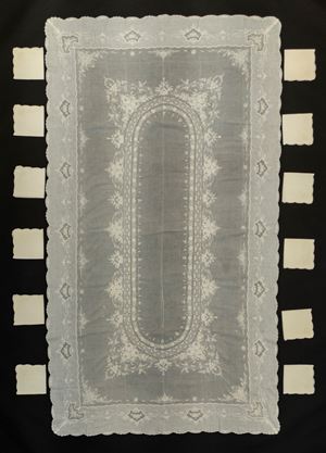 Tovaglia rettangolare in cotone con medaglione centrale di forma ovale decorata a fiori e rose, bordura mossa con riserve a fiori con 12 tovaglioli