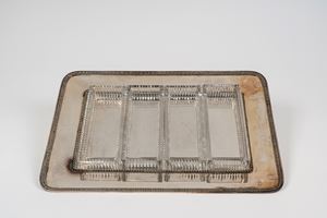 Vassoio porta vivande in metallo argentato di forma rettangolare ad angoli stondati con bordo decorato a palmette, contenitori in cristallo molato.