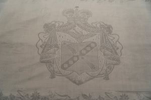 Importante tovaglia in lino decorata con quattro blasoni centrali e motivi floreali lungo il bordo