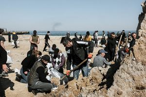 In Odesa, civilians prepare for the 2022 Russian invasion by digging trenches on the beach; smoke from bombardments is visible in the background