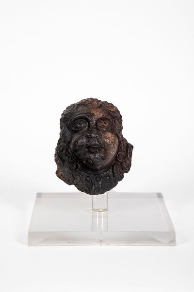 Elemento decorativo in pietra raffigurante volto con capigliatura a riccioli spiraliformi