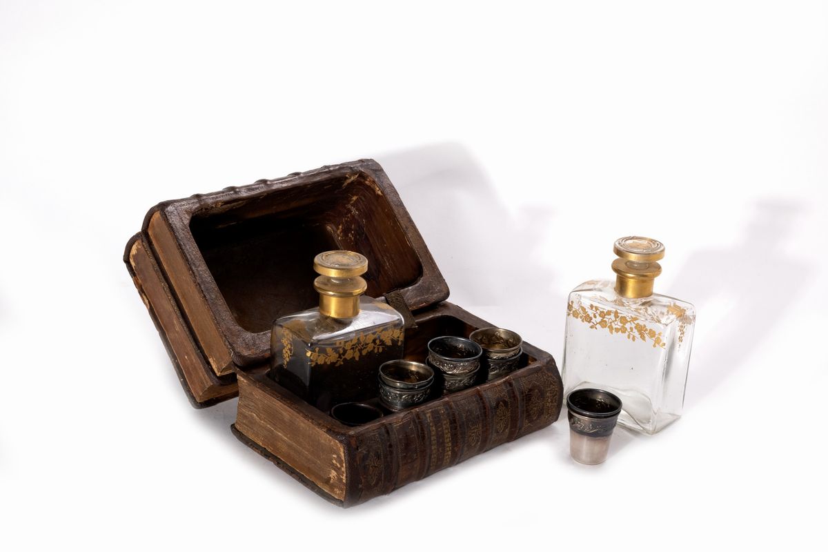 Contenitore a forma di libro con due fiaschette in vetro decorate in oro e otto bicchierini in ar...